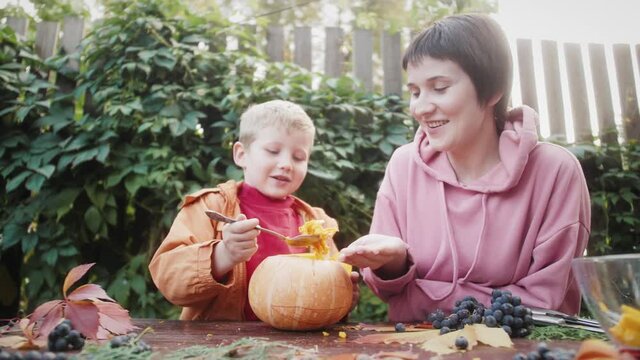 Mom and kid preparing carved pumpkin for Halloween. Holidays and Halloween Decorations Concept. Traditional hobbies in fall and cutting out lanterns from vegetables.