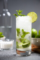 Mojito cocktail on gray table. Some ingredients as background