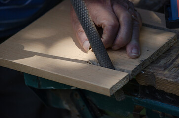Hand of an elderly man who files the surface of the wood with a rasp