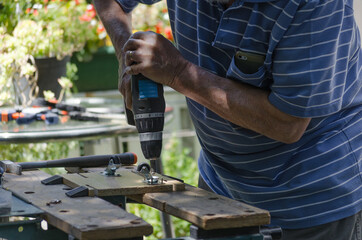 Elderly man making a hole in a piece of wood, using a drill