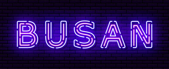 Glowing neon sign with the inscription of the Korean city of Busan. In blue and purple colors. Against a brick wall.