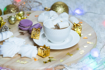 A cup of coffee with milk and marshmallows and garland on wooden salver, other sweets and Christmas decorations around. Concept of New Year presents, festive and holiday