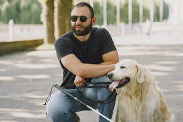 Guide dog helping blind man in the city. Handsome blind guy have rest with golden retriever in the...