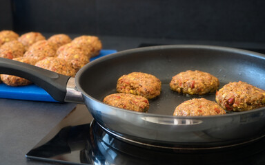 Frikadellen Gemüse Fleisch Paddys mit Kurkuma, Paprika, Linsen, Sesam und Chia Samen beim Anbraten in einer schwarzen Teflonpfanne mit Kokosöl, Produktbild	