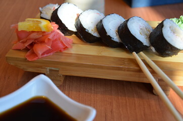 A teenager boy takes sushi roll with Chinese bamboo sticks and drops it into soy sauce, takes a...