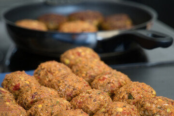 Frikadellen Gemüse Fleisch Paddys mit Kurkuma, Paprika, Linsen, Sesam und Chia Samen beim Anbraten in einer schwarzen Teflonpfanne mit Kokosöl, Produktbild	