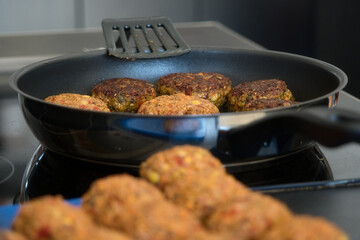 Frikadellen Gemüse Fleisch Paddys mit Kurkuma, Paprika, Linsen, Sesam und Chia Samen beim Anbraten in einer schwarzen Teflonpfanne mit Kokosöl, Produktbild	