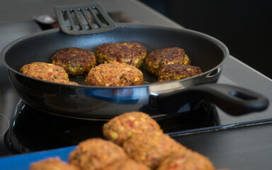Frikadellen Gemüse Fleisch Paddys mit Kurkuma, Paprika, Linsen, Sesam und Chia Samen beim Anbraten in einer schwarzen Teflonpfanne mit Kokosöl, Produktbild	