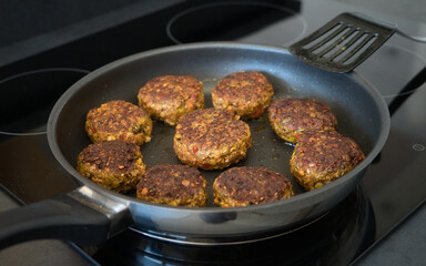 Frikadellen Gemüse Fleisch Paddys mit Kurkuma, Paprika, Linsen, Sesam und Chia Samen beim Anbraten in einer schwarzen Teflonpfanne mit Kokosöl, Produktbild	