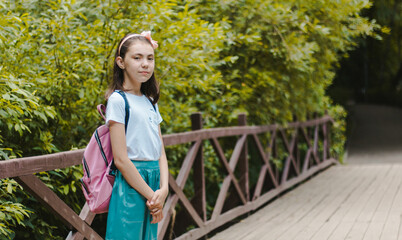 Portrait of a charming girl, smiling in a white t-shirt with a backpack on his back, standing in the open air
