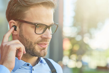 Close up portrait of a young handsome businessman wearing wireless earphones listening to music, enjoying favourite playlist