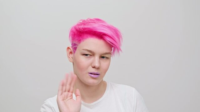 Young beautiful girl with a short haircut and pink hair. A homosexual lesbian model poses on a white background in the studio.
