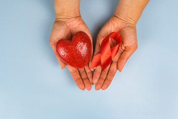 Female hands hold red heart and red ribbon symbol of aids day