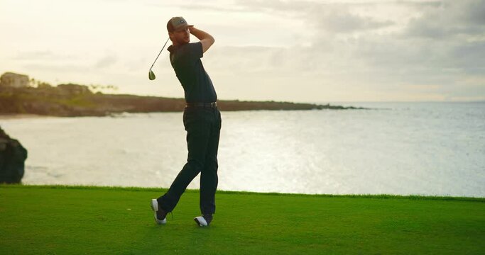 Sunset golf, man swinging and hitting golf ball on beautiful course by the ocean, slow motion