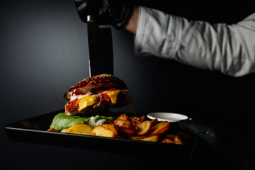 Close up of appetising beef burger. Chef's hands divide into half cooked hamburgers from beef. Street food ready to serve on a food stall. Chef cooks an American tasty hamburger.