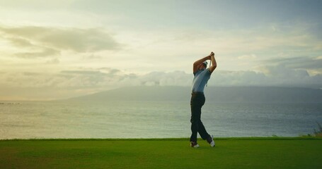Sunset golf, man swinging and hitting golf ball on beautiful course by the ocean, slow motion