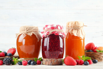 Sweet jam in glass jars with ripe berries on white background