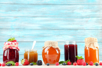 Sweet jam in glass jars with ripe berries on blue background