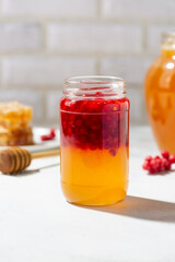 Jar of honey with red chisandra chinensis berries on light table. Healthy food.