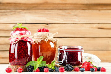 Sweet jam in glass jars with ripe berries on brown wooden table