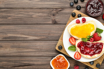 Toasts with jam and ripe berries on wooden table