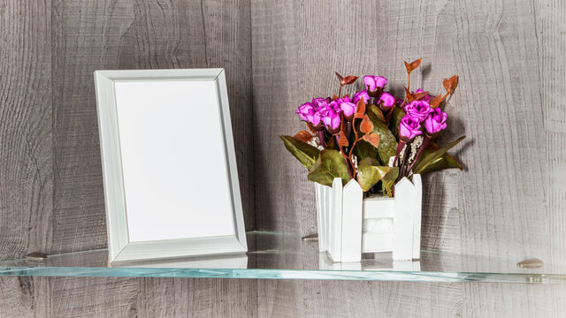 vertical photo frame with mockup empty place stand on glass shelf near wooden flowerpot with flowers