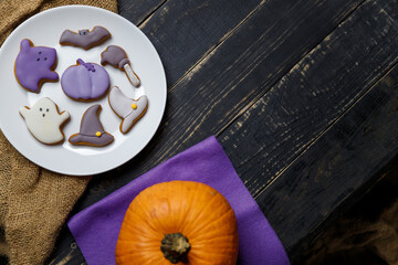 Pumpkin and Halloween cookies on white plate, sackcloth on black wooden background. Hallooween trick or treat concept. Copy space.