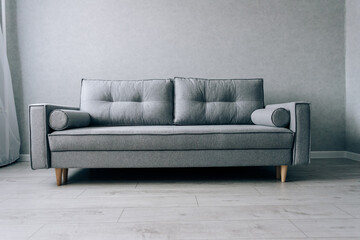 Modern grey sofa with wooden legs in the room
