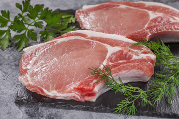Raw pork steak on a dark background with herbs.