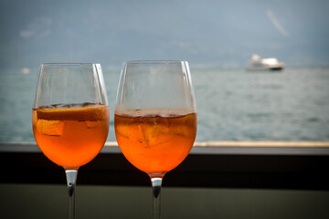 Two glasses of Aperol Spritz standing on table with beautiful view on Lake Garda and Alps