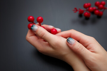 Female hands with fir-tree forest manicure holding red berries on black background. Christmas or winter nail art. Hands care, fingernails design, beauty and health concept. Copy space.
