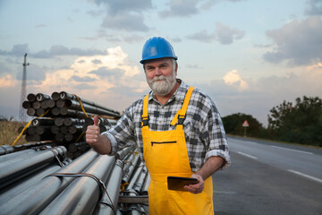 Smiling worker with tablet in hand and heap of insulated pipes for natural gas