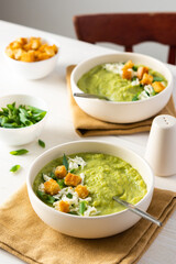 Healthy delicious broccoli and cucumber cream puree soup with mozzarella, green onions and croutons, bowl of soup on a white table