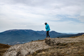 woman tourist in a blue jacket on the top of the mountain at the level of floating clouds