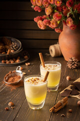 Refreshing delicious melon smoothie with cinnamon, hazelnuts and chocolate, vase of chrysanthemums and glasses of smoothie on wooden background