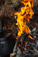 Tourist kettle, kettle in the fire of a burning campfire in a camping trip. Cooking food in the forest on wooden wood during the hike. Active rest and entertainment in nature.
