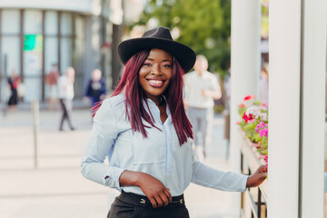 smiling young African American girl with pink hair wearing a hat walking down the street on a sunny day.