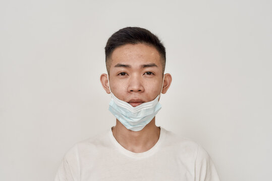 Portrait Of Young Asian Man With Medical Mask On His Chin Looking At Camera Isolated Over White Background. Health Care, Prevention, Safety Concept