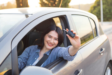 Happy woman with car key sitting in modern auto outdoors on sunny day. 