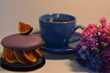 
Delicious dessert of purple macaroons, whipped cream and figs, next to coffee in a blue mug and limmonium flowers