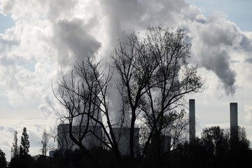 Backlit shot of cooling towers and chimneys with steam clouds of a power plant and silhouettes of...