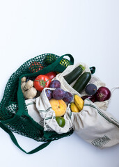 Vertical image of different kinds of ecological bags full of healthy, colorful and vegan fruits and vegetables centered on a white background. A wide white space remains at the top.