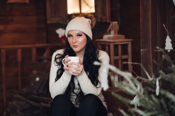 Portrait of stunning long-haired woman with smokey eyes in warm hat drinking hot tea or cacao on...