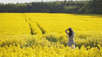 Scenic view of vibrant yellow rapeseed field with young woman in transparent dress