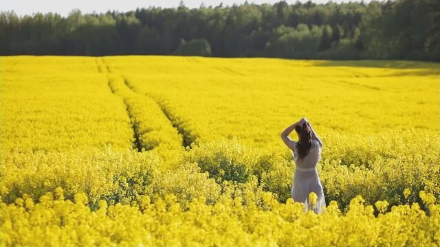 Scenic view of vibrant yellow rapeseed field with young woman in transparent dress