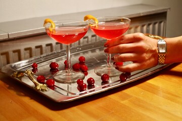 Hand reaching for two cosmopolitan cocktails garnished with cranberries