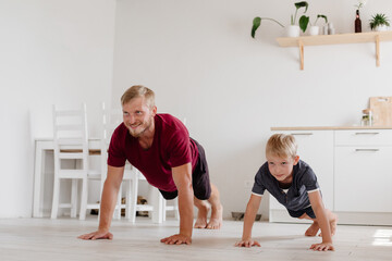 Father and son play sports in the bright kitchen at home. Home workouts. Stay home. Family concept. A man and a boy are doing push-ups.
