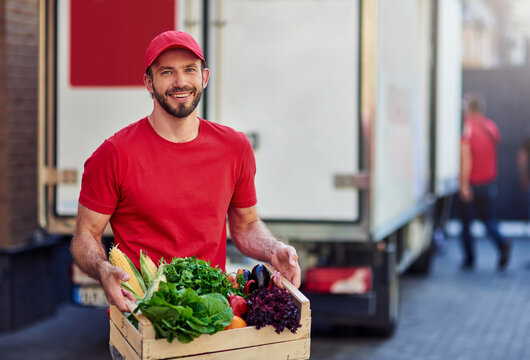 Young cheerful caucasian male courier holding grocery in box