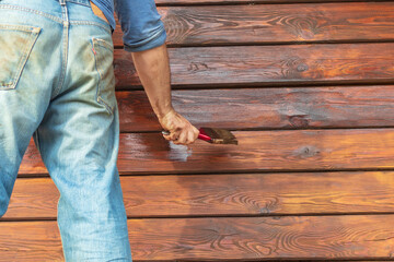 Daylight. a person with the help of a brush applies to the facade of a wooden house, a special agent to extend the life of the building.