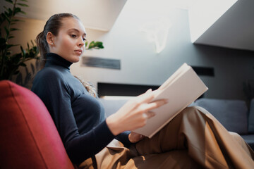 lonely blonde woman of Caucasian appearance is reading a romantic fairy tale book. An interesting edition of the new story. Sits in a comfortable chair